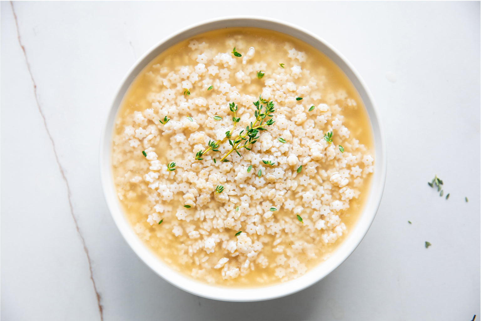 Bowl of jovial brown rice stelline in soup with thyme leaves