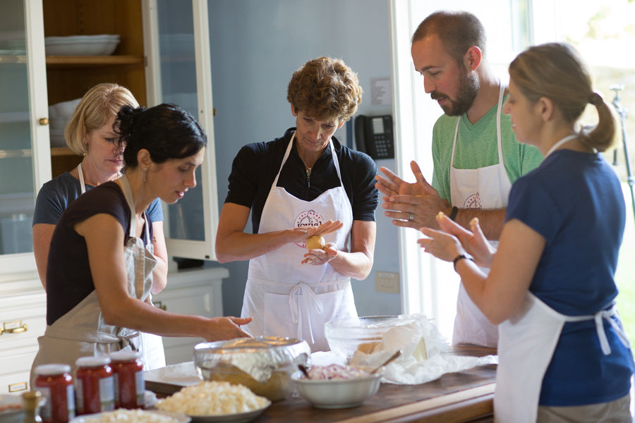 Five people in aprons around a kitchen island shaping dough and preparing ingredients