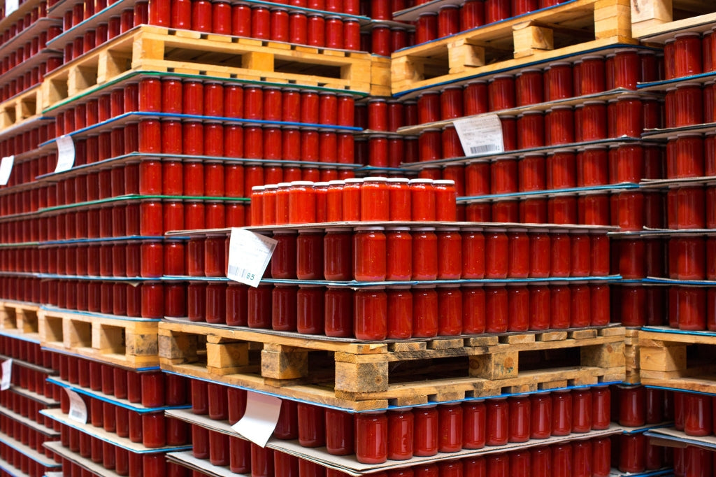 Rows of red tomato-sauce jars on wooden pallets in a warehouse storage area