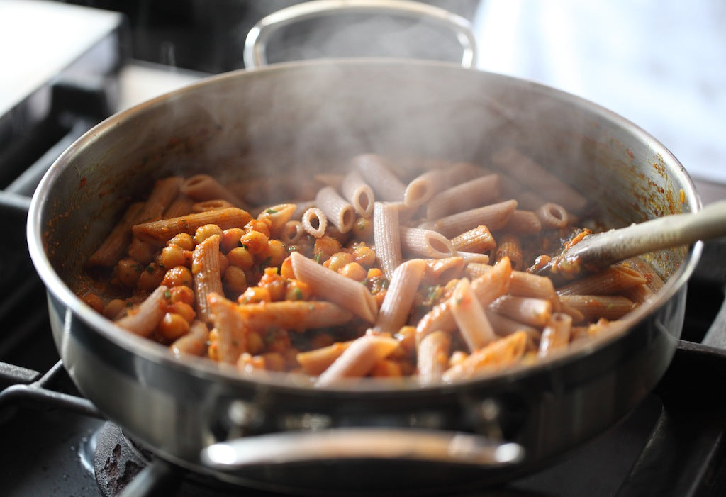 Einkorn penne tossed with spicy Moroccan chickpeas in a steaming stainless-steel skillet on a stovetop