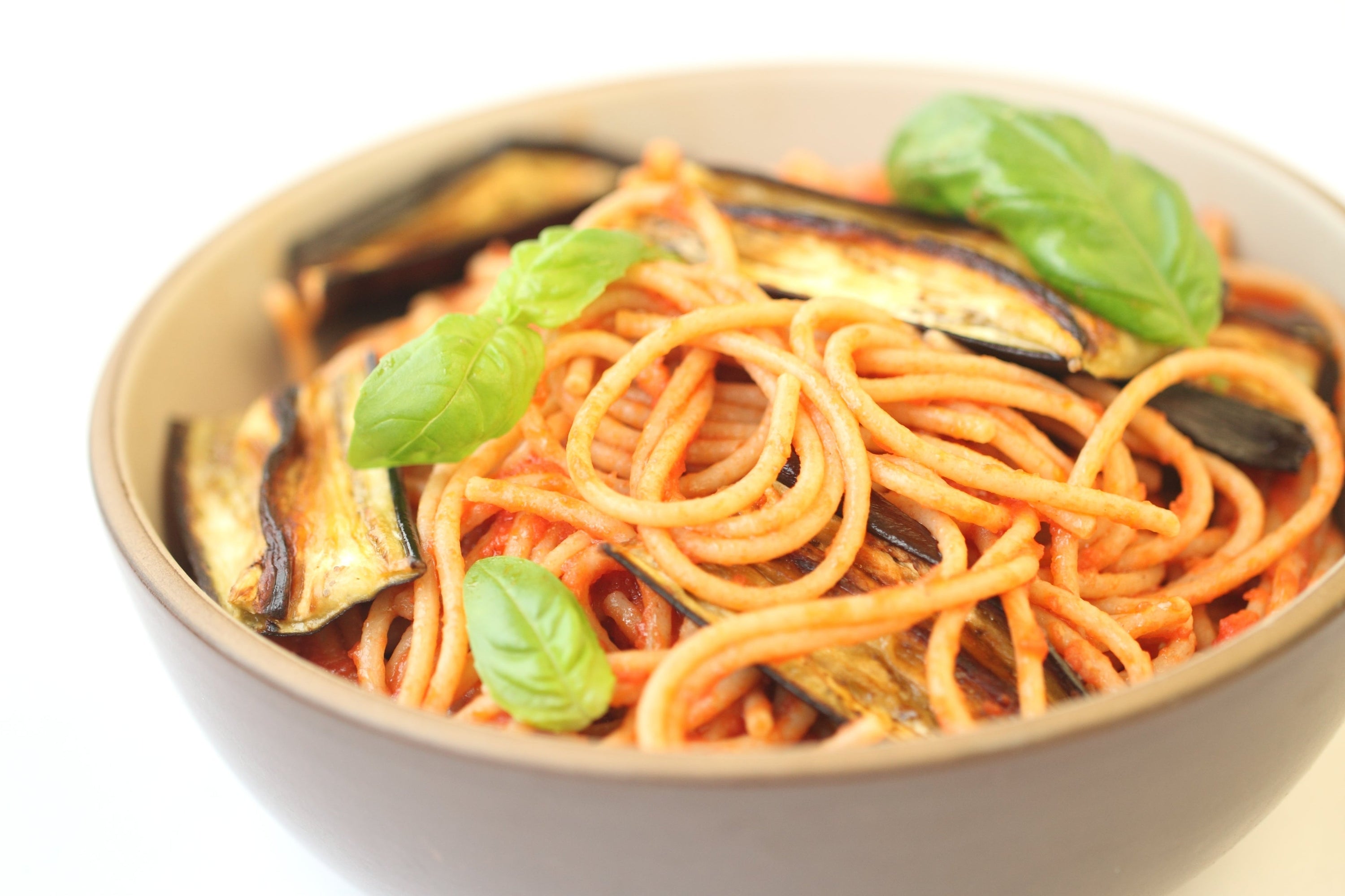 Bowl of spaghetti in tomato sauce topped with roasted eggplant slices and fresh basil