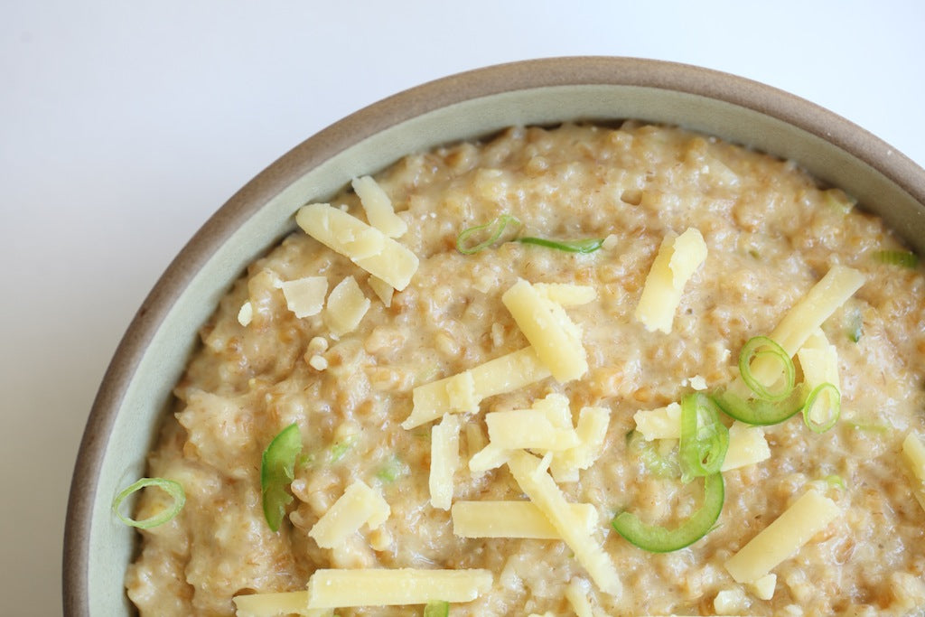 Bowl of jalapeño cheddar einkorn polenta served close-up, topped with shredded cheddar and sliced jalapeño on a white background