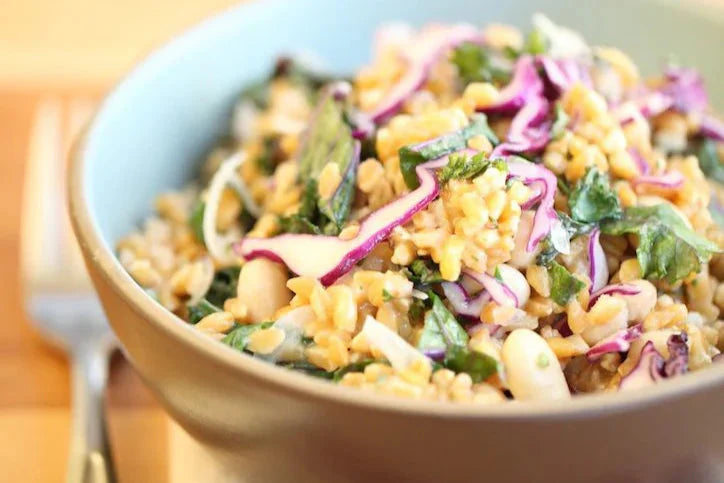 Bowl of cooked einkorn with chopped kale and shredded red cabbage served on a wooden table with a fork in the background