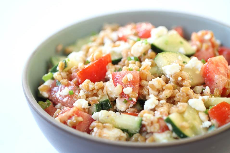 Einkorn wheat berry salad served in a gray bowl with chopped tomatoes, cucumber, scallions and crumbled feta