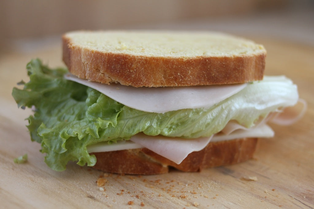 Einkorn sandwich with turkey and green leaf lettuce sitting on a wooden cutting board