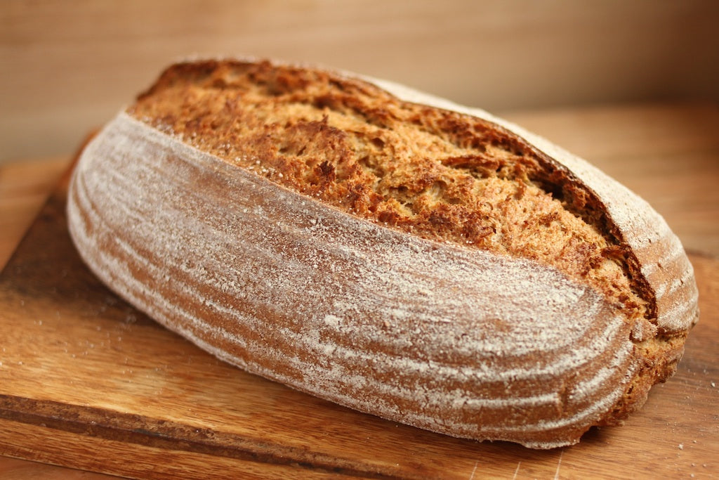 Three-quarter view of whole-grain Einkorn sourdough batard with deep scored crust and floured patterned sides on a wooden cutting board