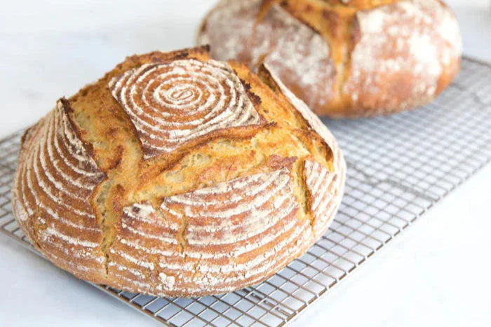 Three quarter view of einkorn sourdough boules showing golden crust, spiral flour pattern and deep scoring on a cooling rack with white background