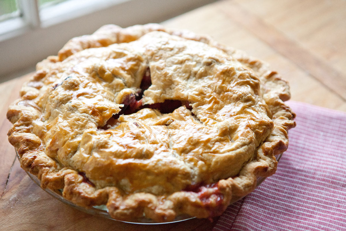 Three-quarter view of a spiced apple and cranberry pie with an Einkorn golden flaky crust on a wooden board