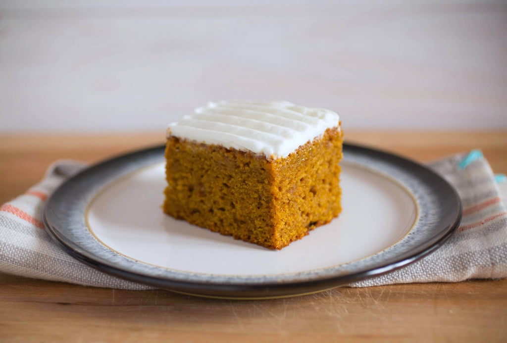 Three-quarter view of apple-squash einkorn spice cake slice showing moist crumb and white frosting on a plate with striped linen