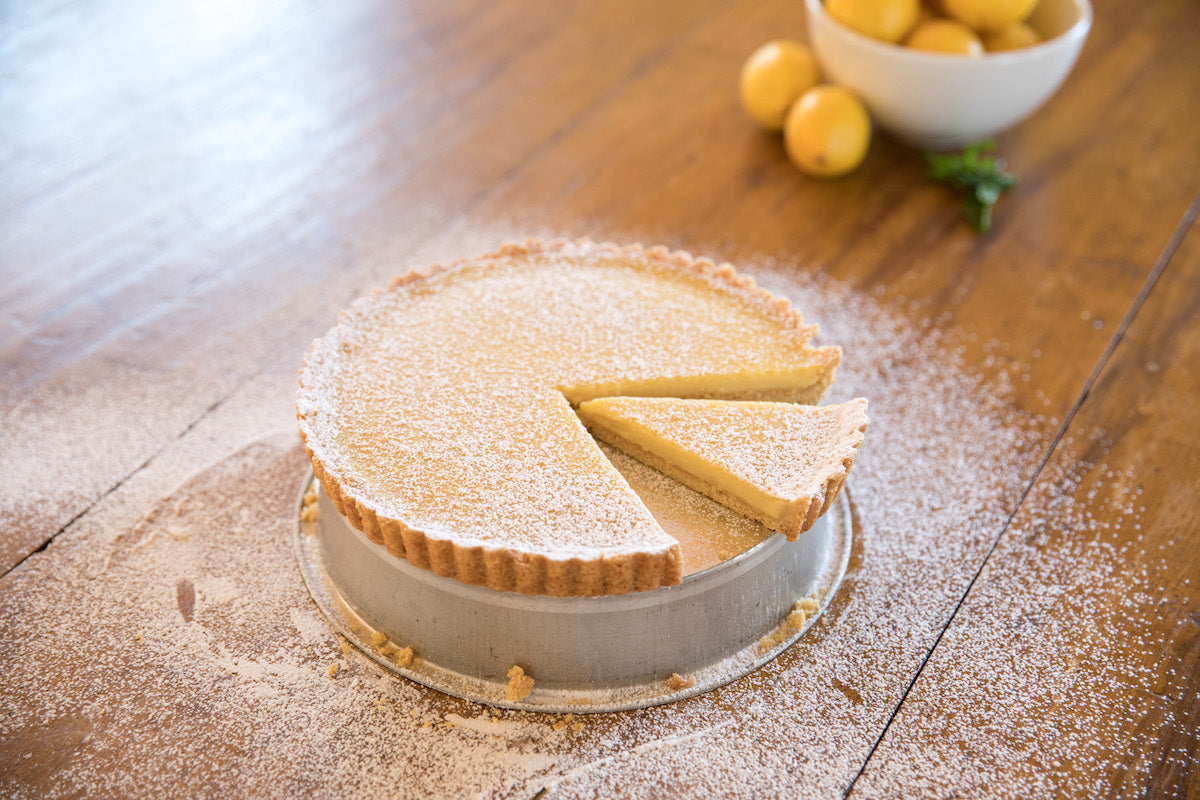 Three-quarter view of Einkorn lemon cream tart with one slice removed, dusted with powdered sugar on a wooden table
