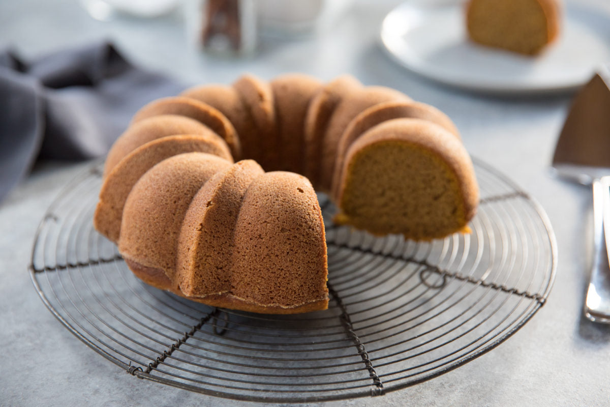 Front-left view of Einkorn pumpkin spice Bundt cake with one slice removed on a wire cooling rack and gray tabletop