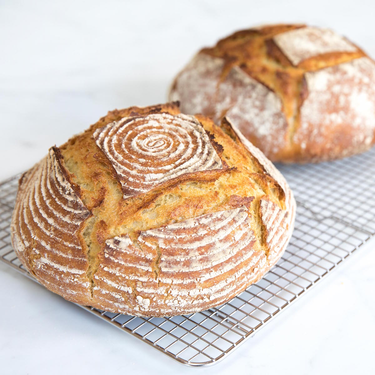 Front view of two Einkorn sourdough boules showing golden crust and banneton spiral flour pattern on a wire cooling rack