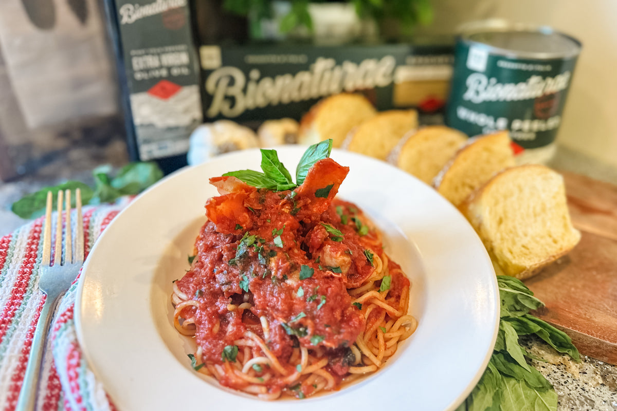 Spaghetti in lobster tomato sauce topped with basil, served with toasted bread and a Bionaturae box in the background