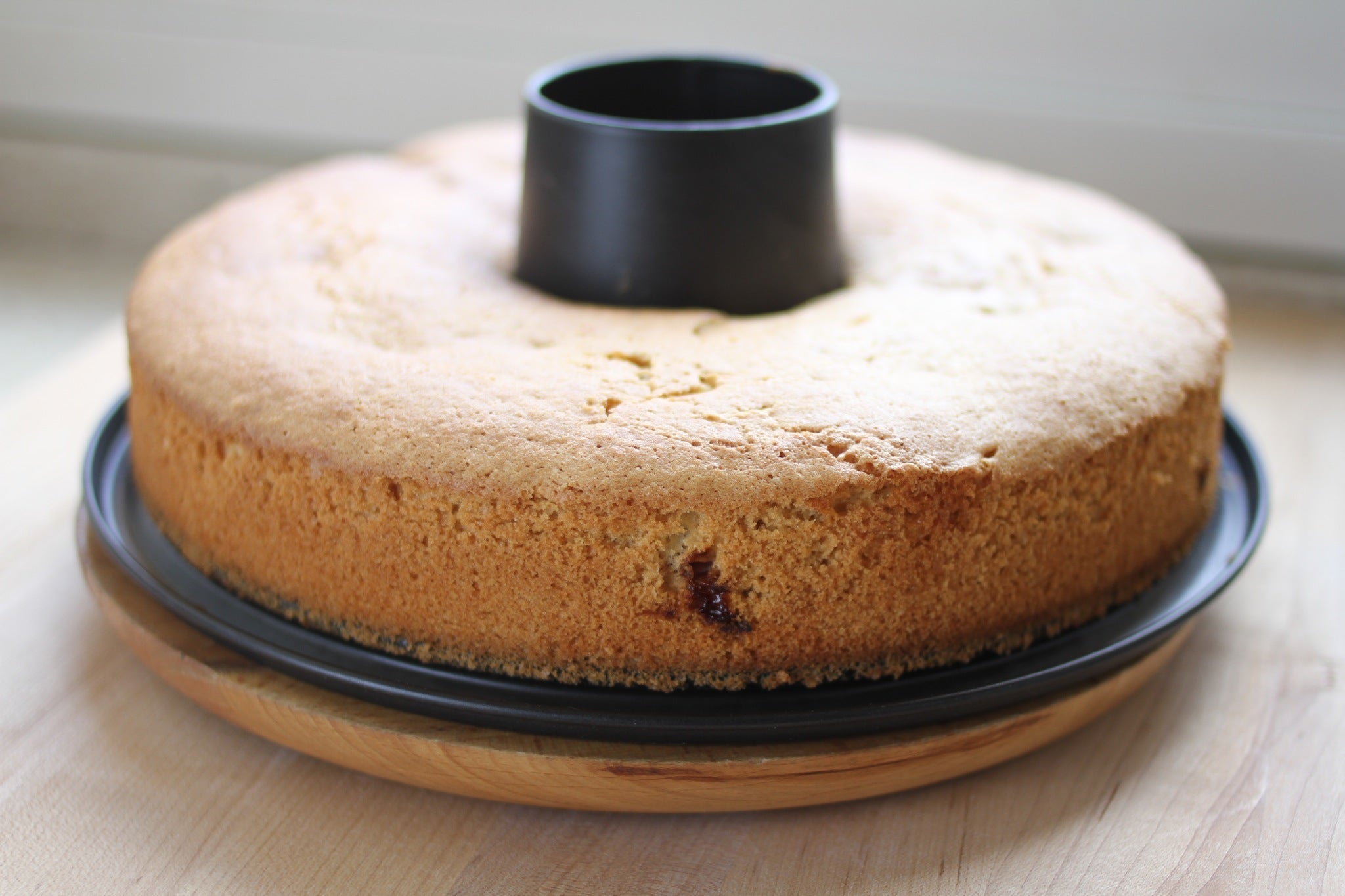 Side view of olive oil cake showcasing golden-brown crust in a tube pan on a wooden board with soft window light background