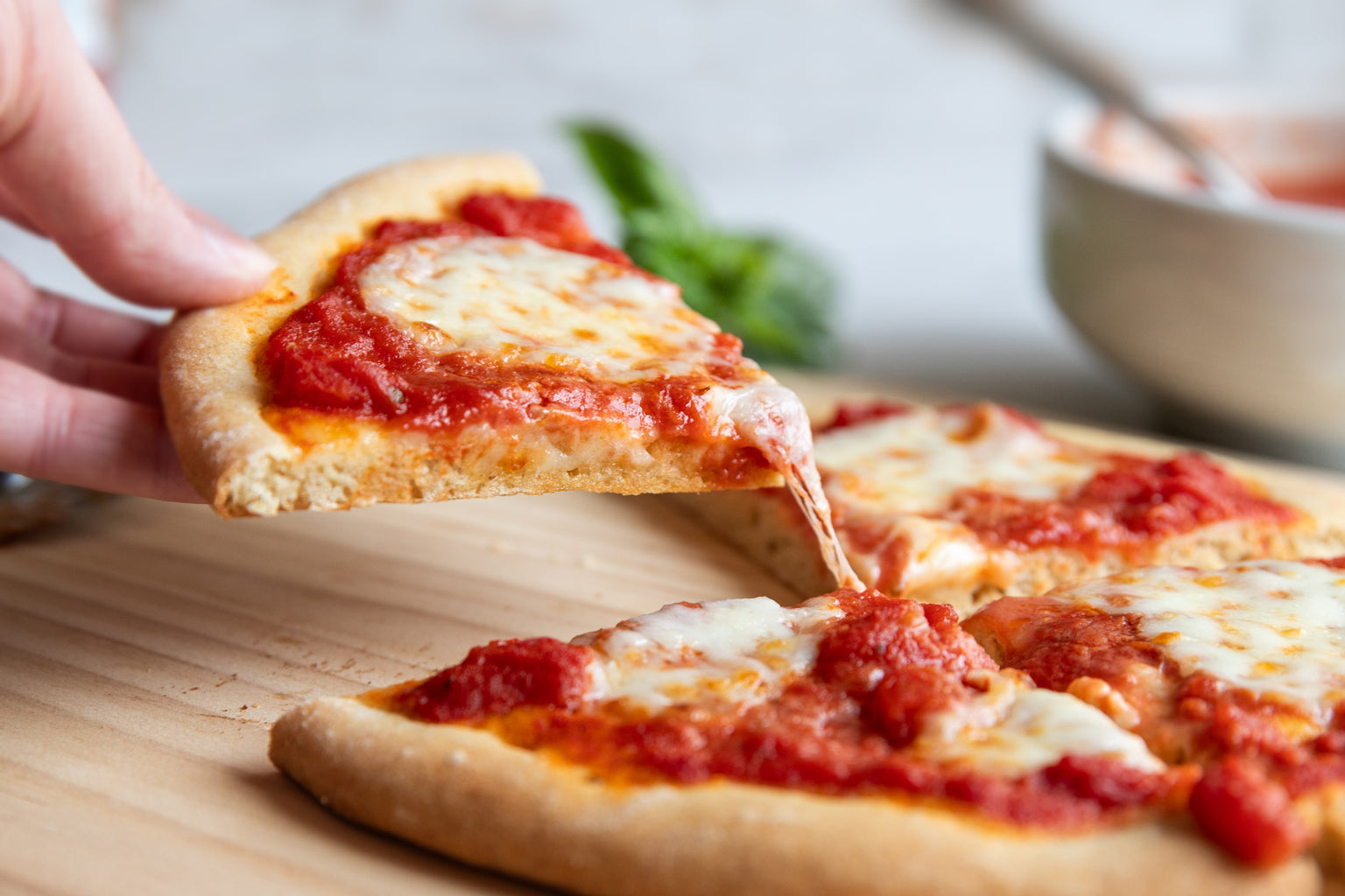A slice of freshly baked einkorn pizza being picked up, with strings of melty mozzarella cheese stretching from the pizza
