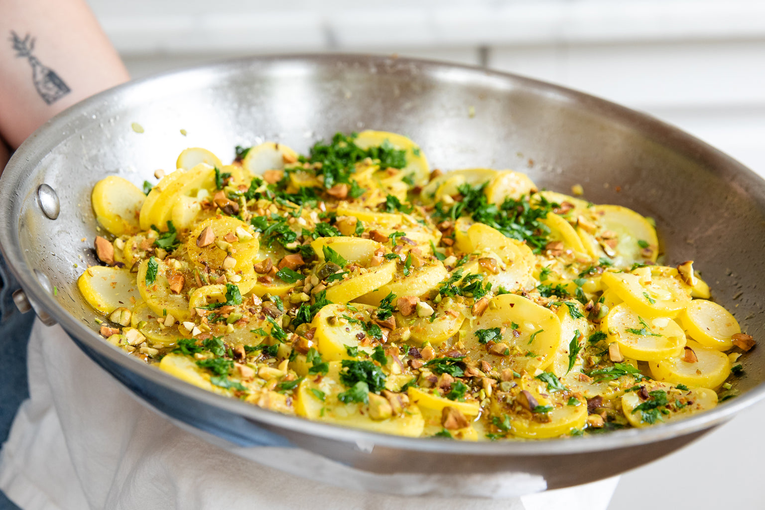 A skillet full of hot summer squash with chopped pistachios and parsley