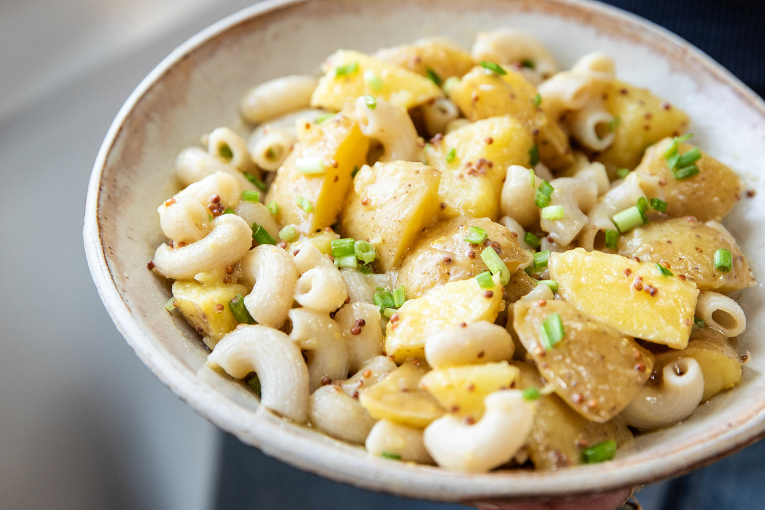 A bowl of Tangy Potato Pasta Salad, made with jovial Brown Rice Elbows and sprinkled with freshly chopped scallions