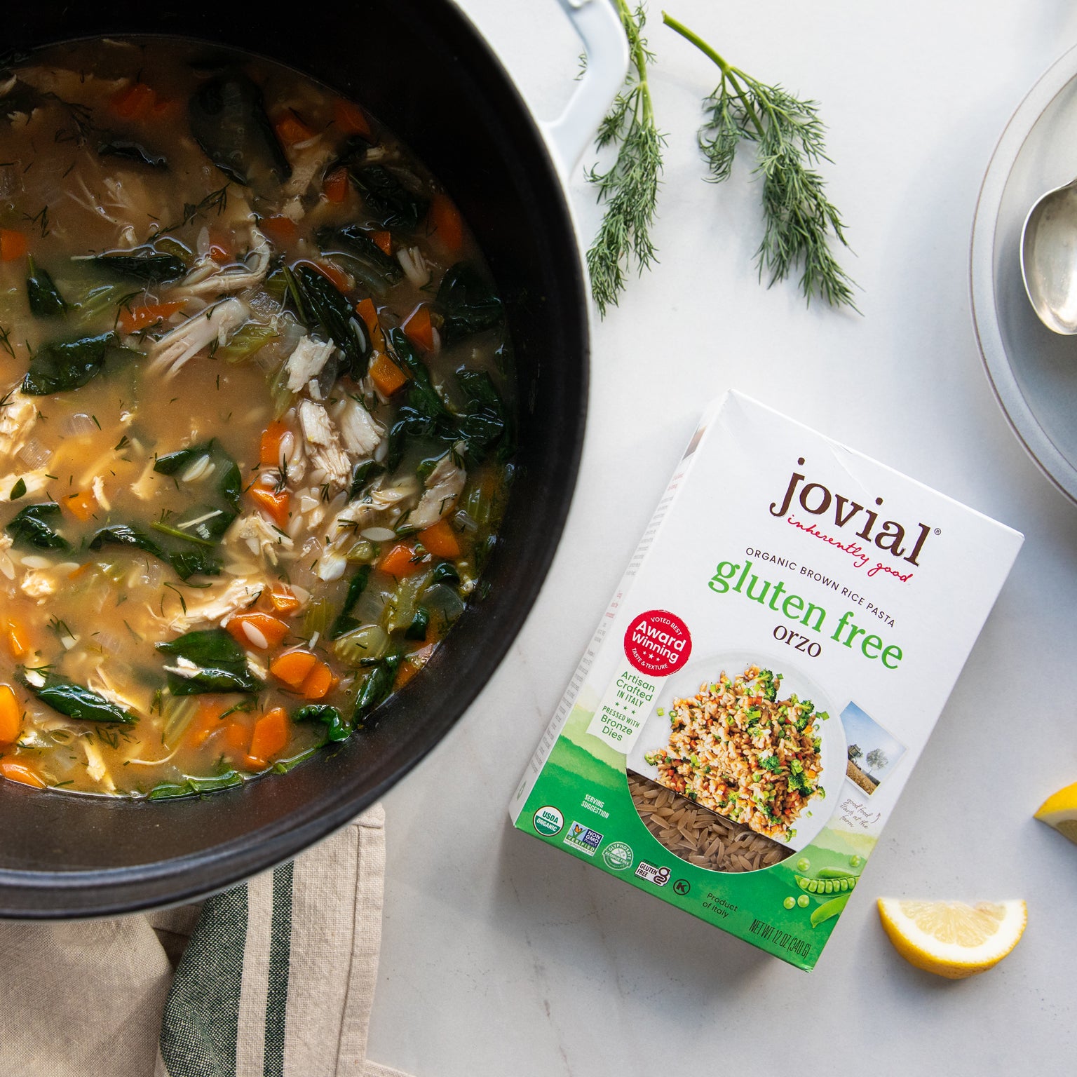 Pot of Lemon Chicken orzo soup next to a box of Jovial Brown Rice Orzo